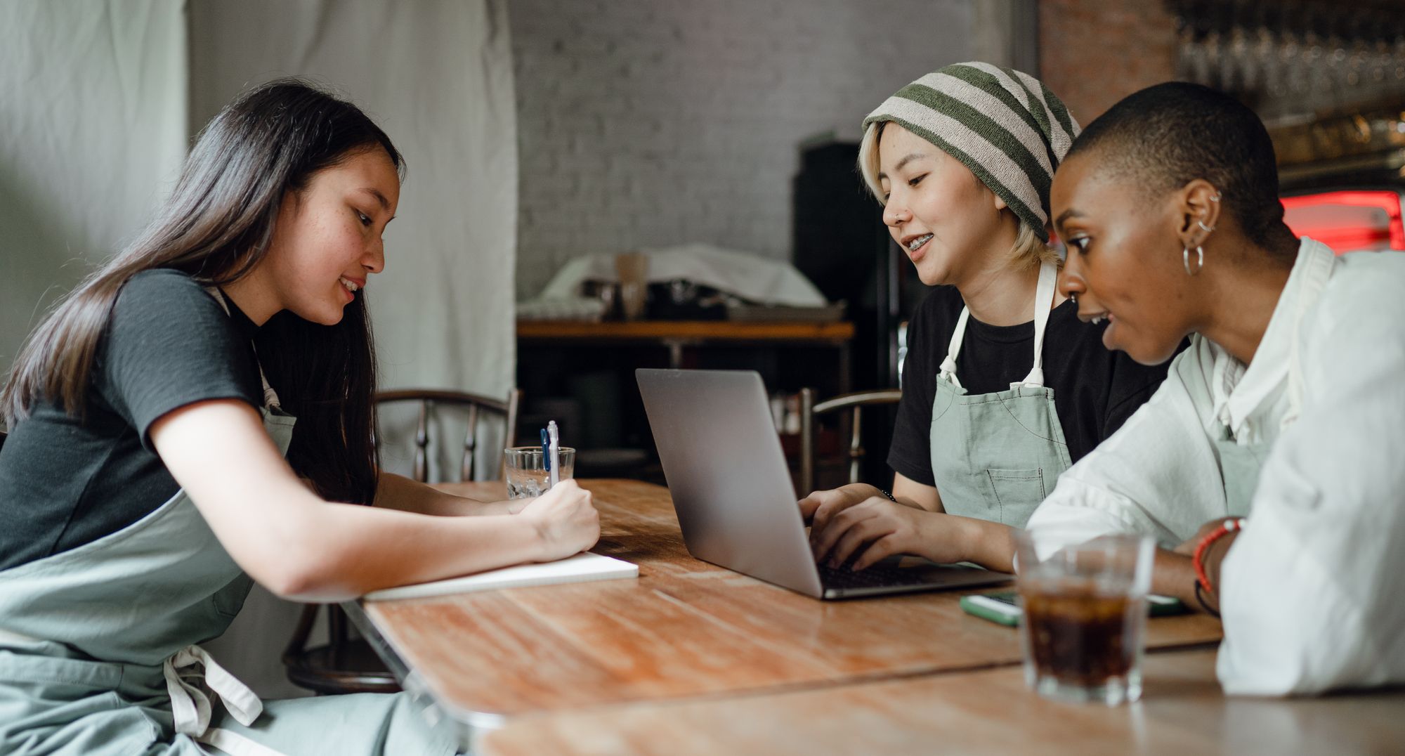 Three collaborators smiling, taking notes, and working together around a laptop