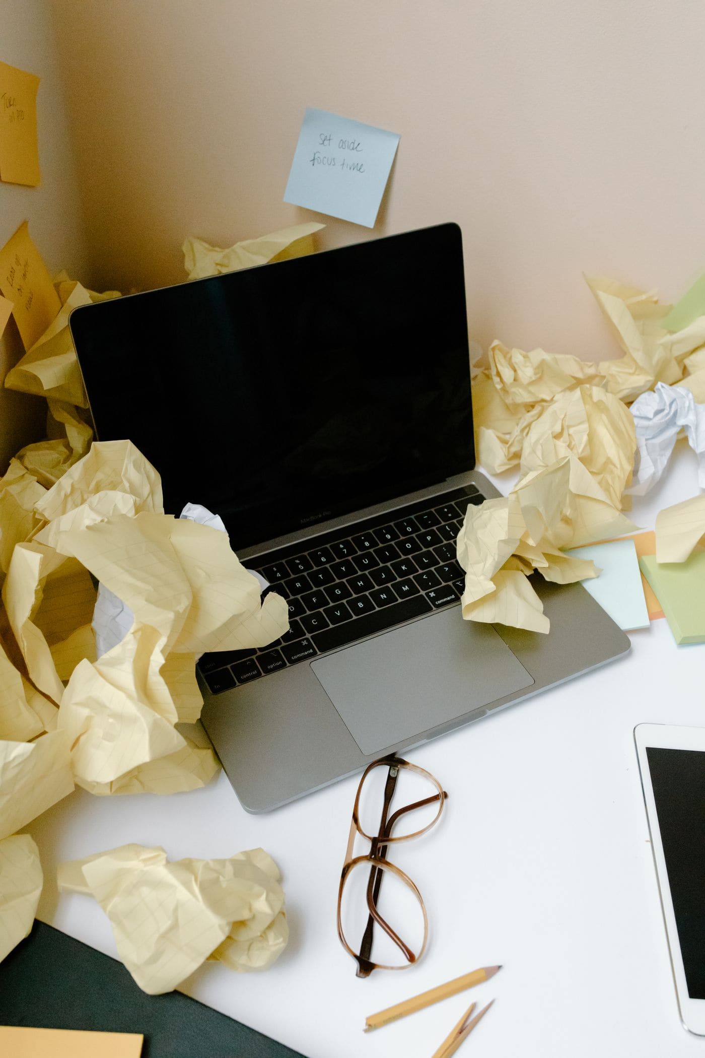 A laptop surrounded by crumpled papers and scattered notes